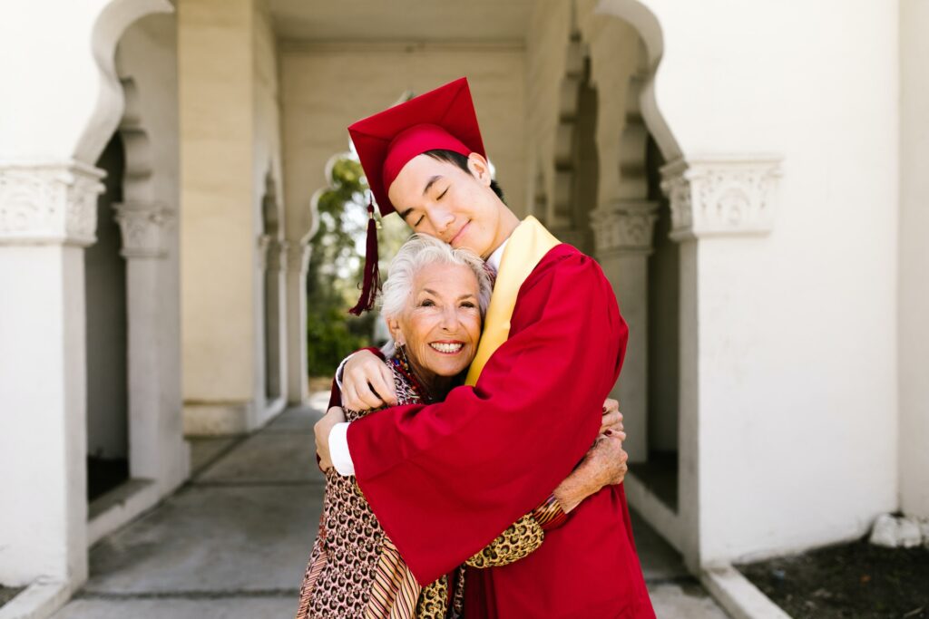 grandmom hugging grandson in red cap and gown graduation day