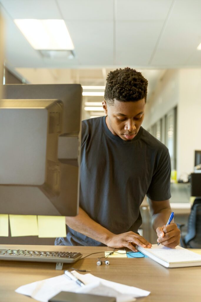 Man at computer station, standing up, entering journal entries in his Black owned business for a Black Business Month post