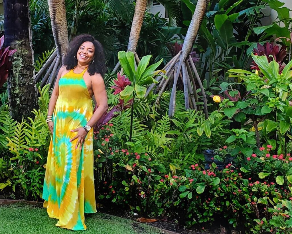 Nicole Commissiong in a floral dress, with curly hair and in the a backdrop