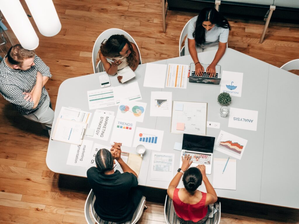 overhead photo of a team of workers at a table going over a report and charts in blog article about the importance of employers taking care of their employees in order to survive post pandemic shortage